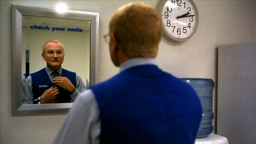 Robin Williams adjusting his tie in the mirror underneath a sign reading "Check your smile."